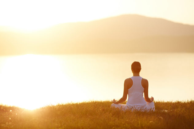 Woman sitting in lotus position on green grass in front of the mountains